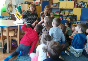 Dzieci siedzą na dywanie, panie czytają im książkę o przygodach Koziołka Matołka